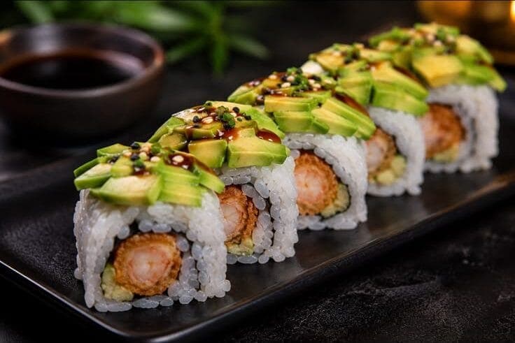 Rangée de makis uramaki garnis de tranches d'avocat et nappés de sauce teriyaki sur ardoise