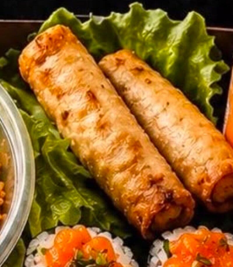Deux rouleaux de printemps frits dorés posés sur une feuille de laitue, accompagnés de riz