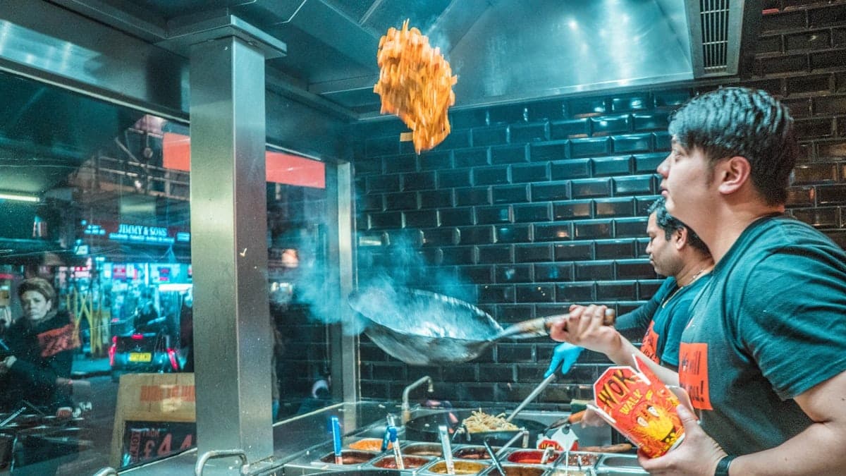 Cuisinier faisant sauter des légumes au wok dans l'ambiance nocturne d'un food court