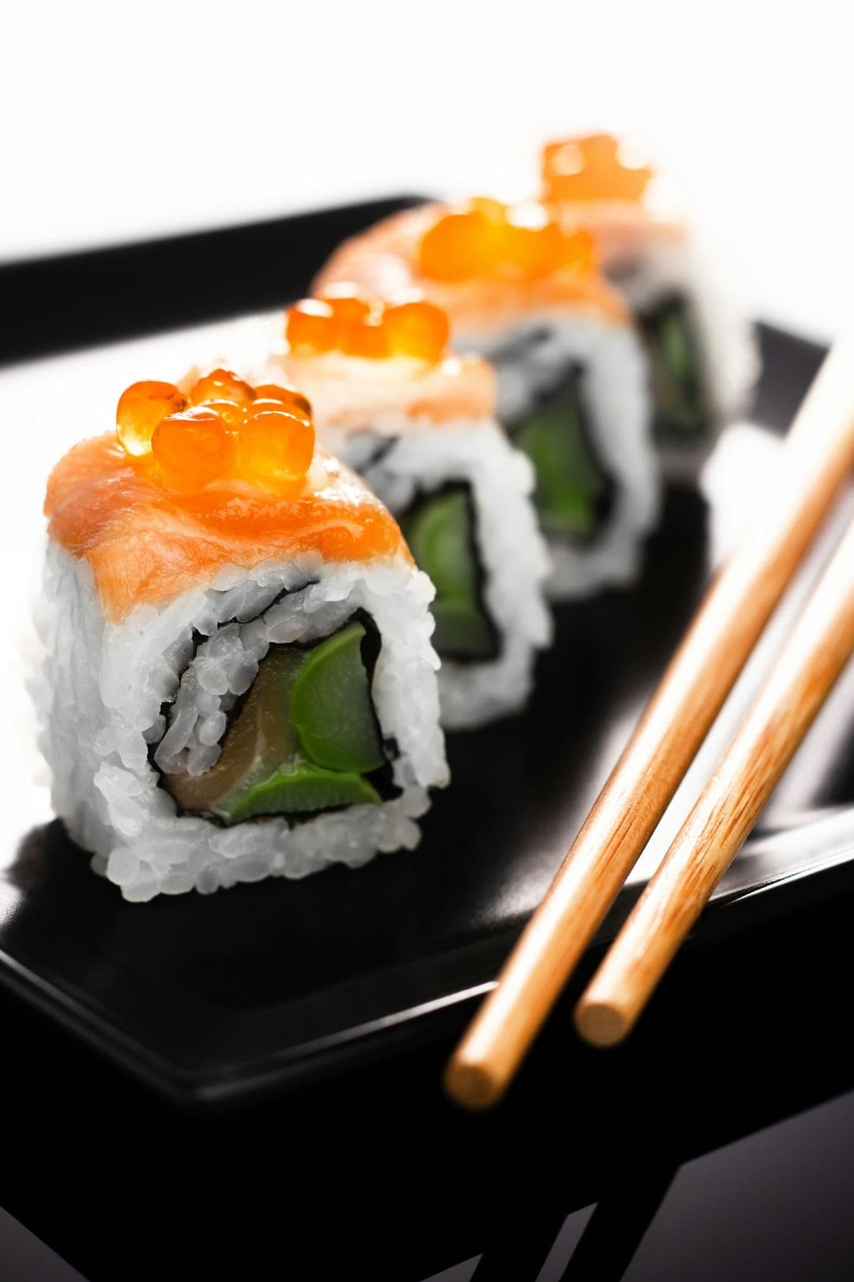 Rangée de makis california garnis de saumon et d'œufs de poisson sur un plateau noir laqué